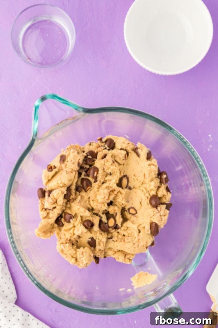 Vanilla cookie dough generously studded with chocolate-covered almonds and toffee bits, showcased in a mixing bowl.