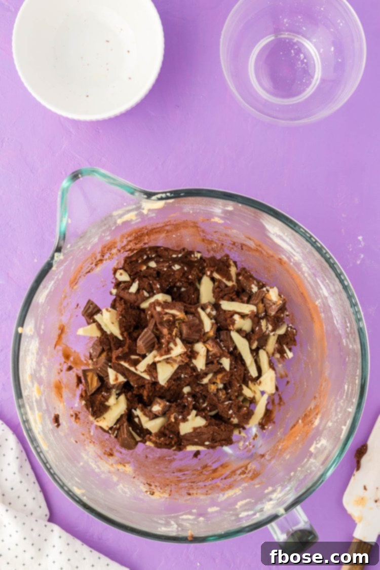 Decadent chocolate cookie dough filled with chopped white chocolate and peanut butter cups, ready for baking.