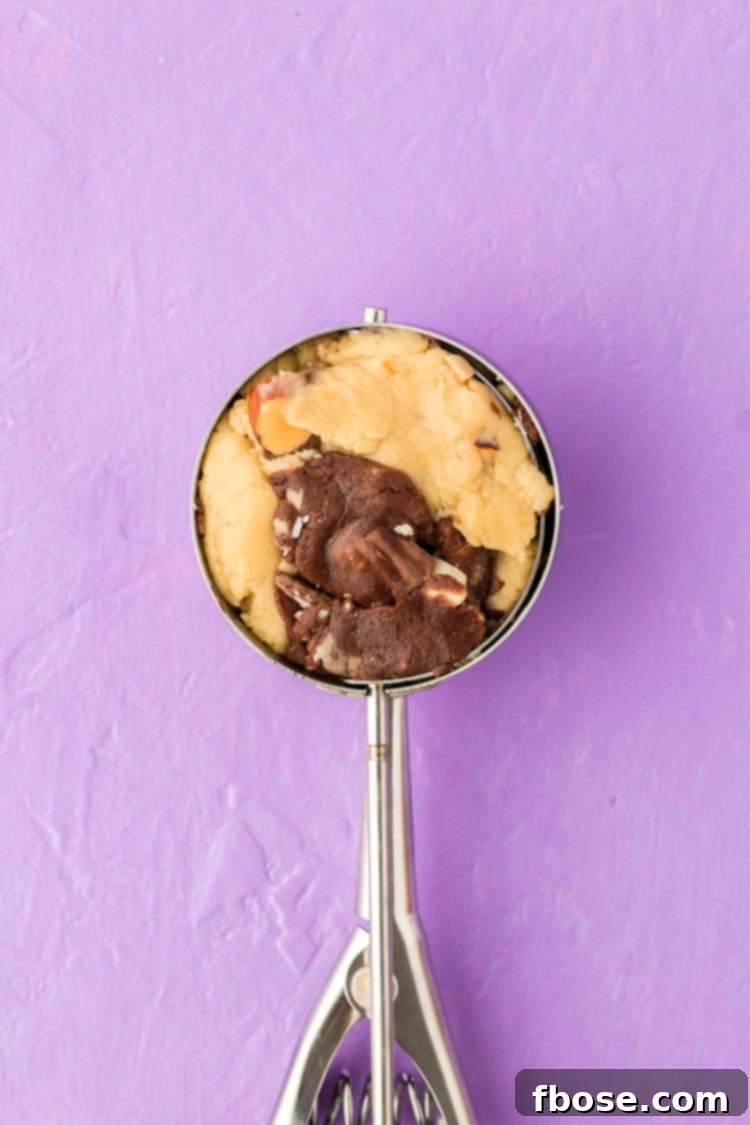 A scoop filled with marbled vanilla and chocolate cookie dough, ready to be placed on a baking sheet, showcasing the swirled pattern.