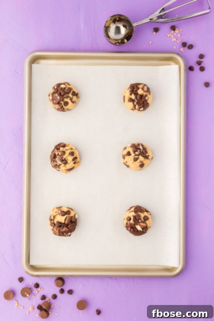 Balls of marbled vanilla and chocolate cookie dough evenly spaced on a parchment-lined baking sheet, prepared for the oven.