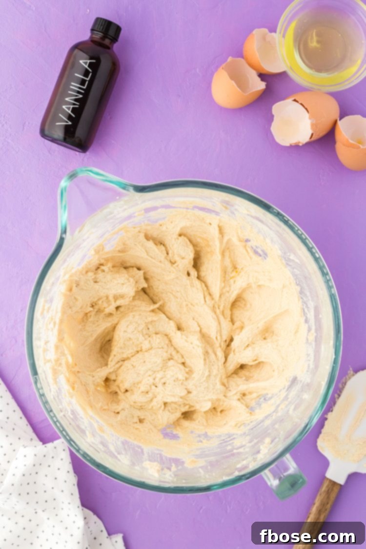 The initial stages of cookie dough formation in a glass bowl, showing the wet ingredients smoothly combined before dry ingredients are added.