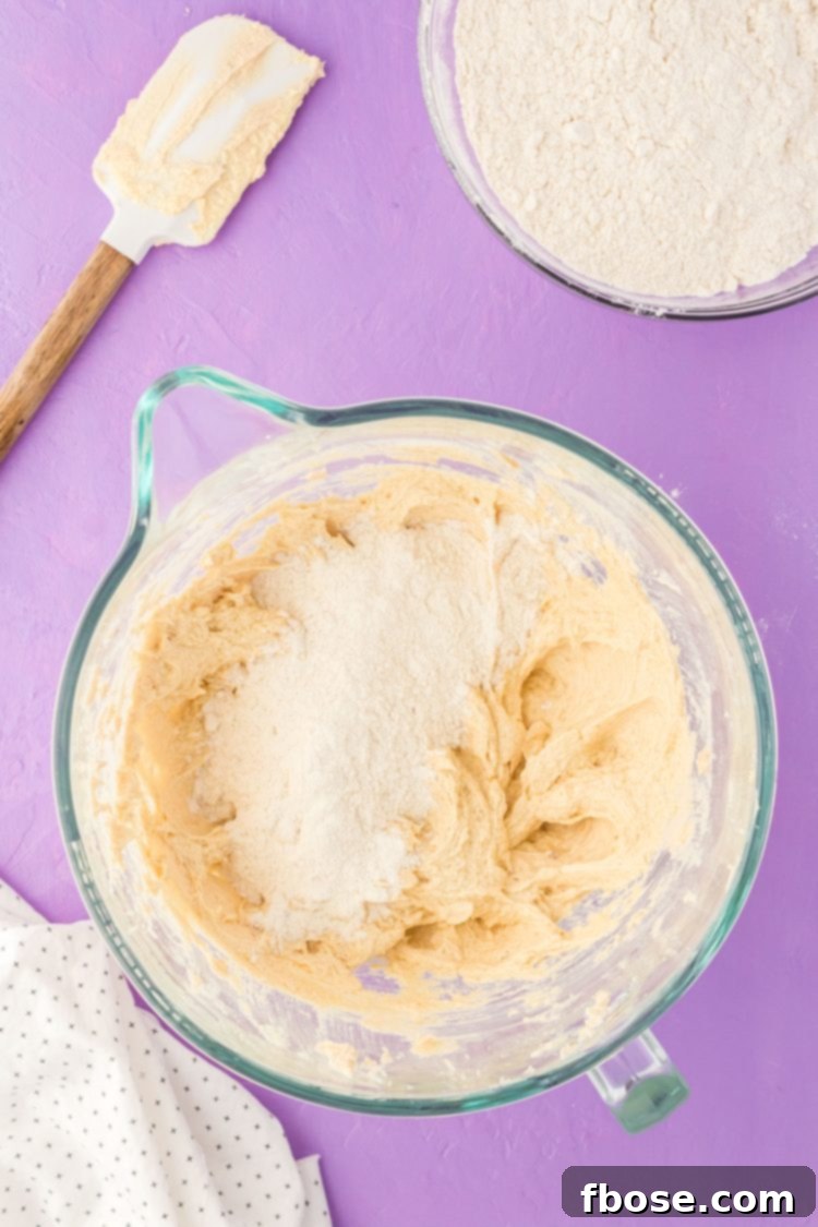 Dry ingredients being gradually incorporated into the wet cookie dough mixture, forming a cohesive base.