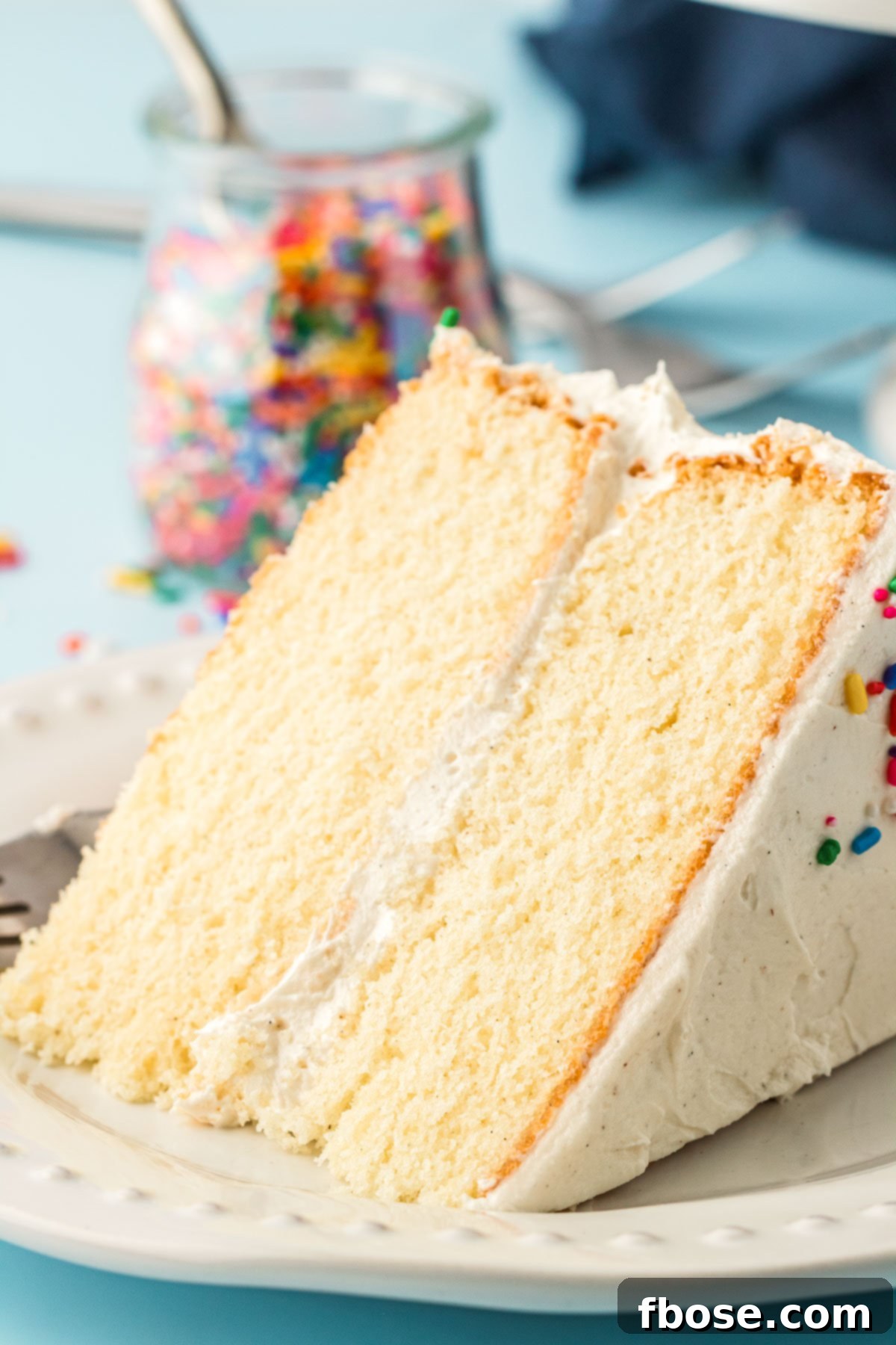 A perfectly sliced piece of white vanilla cake on a pristine white plate, showcasing its tender crumb and delicate vanilla bean specks.