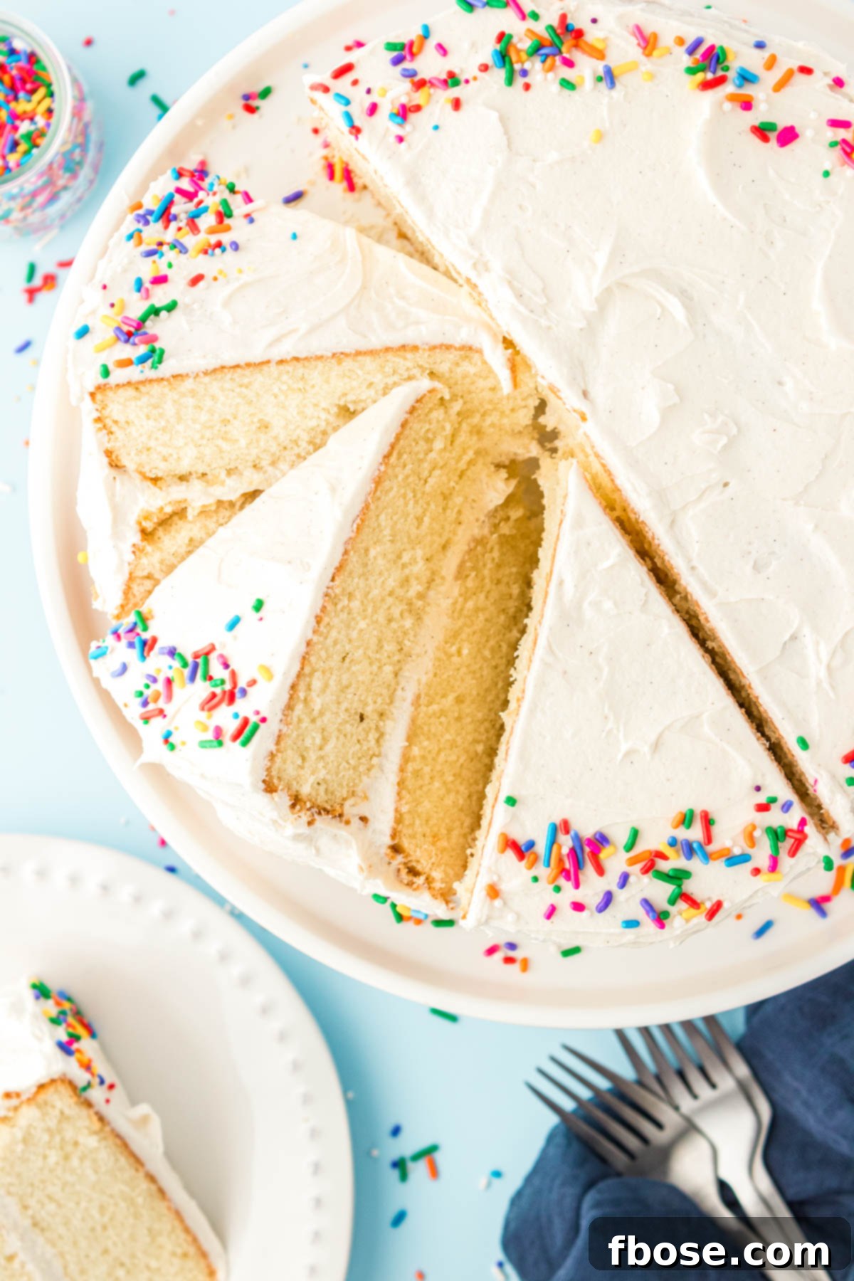 An overhead view of a beautifully assembled white layer cake, with several slices already cut and leaning, showcasing the moist interior.