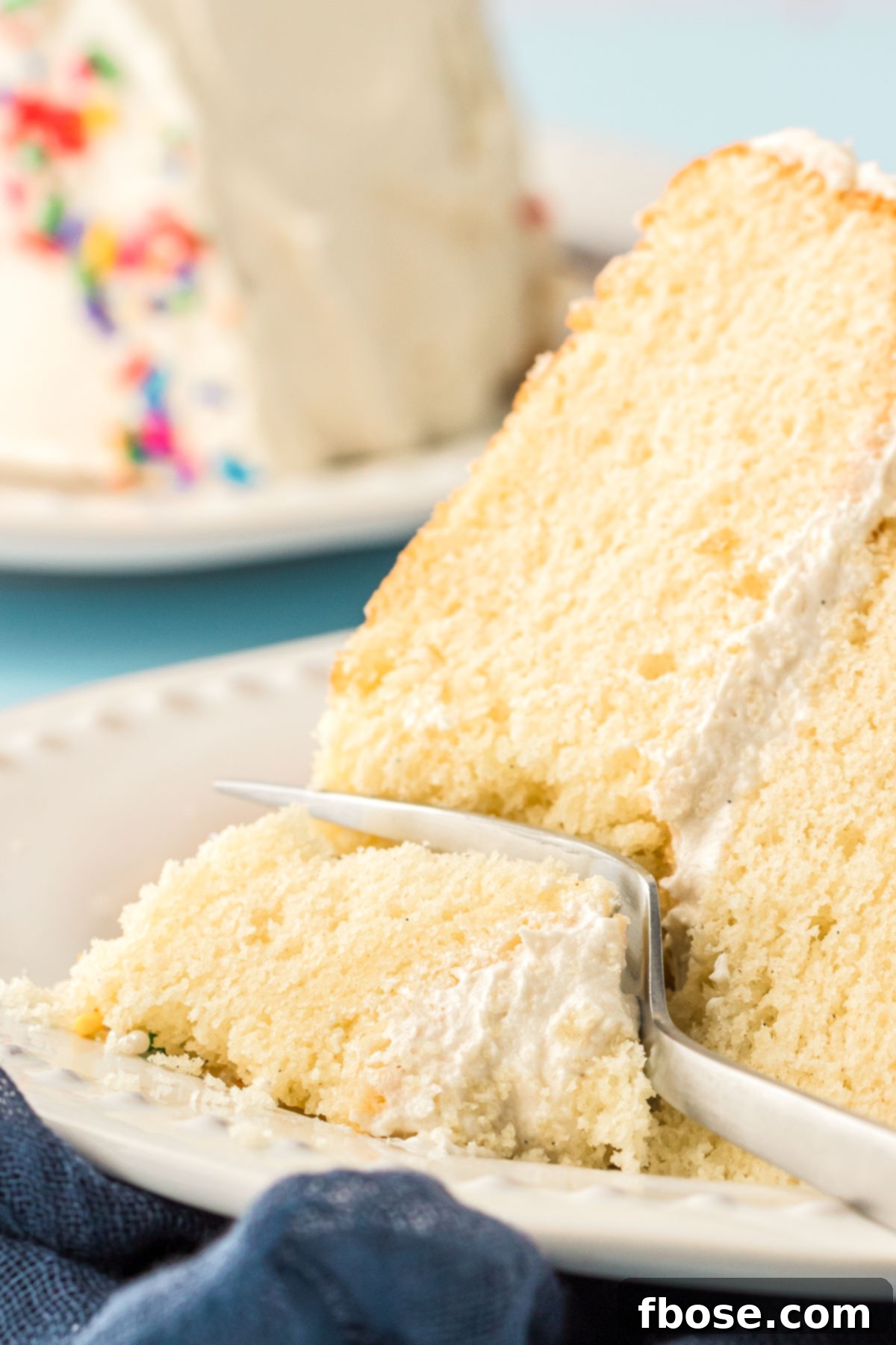 A fork taking a delicious bite out of a soft, fluffy piece of white vanilla cake, showing its moist interior.