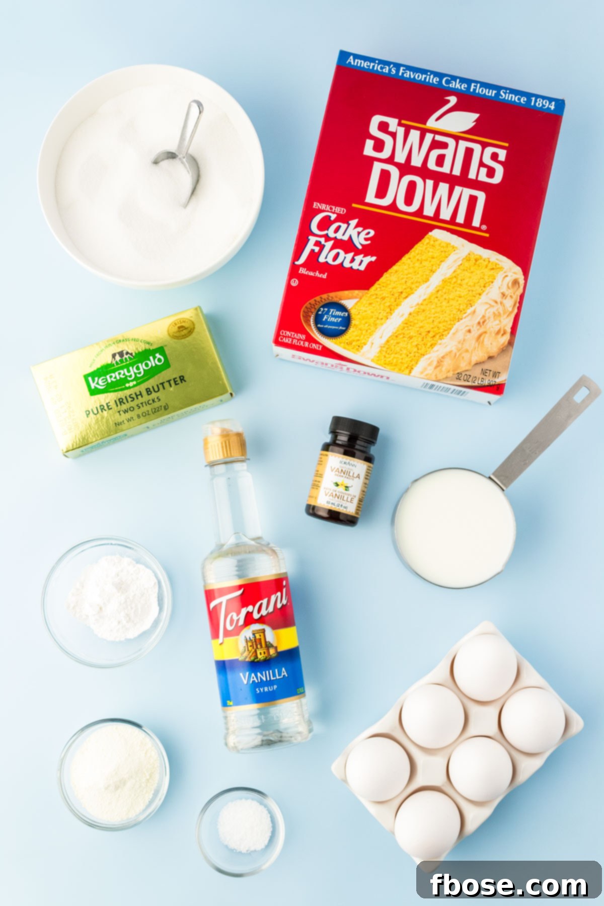 An overhead shot showcasing all the fresh, high-quality ingredients neatly arranged on a blue surface, ready to be combined for the vanilla white cake.