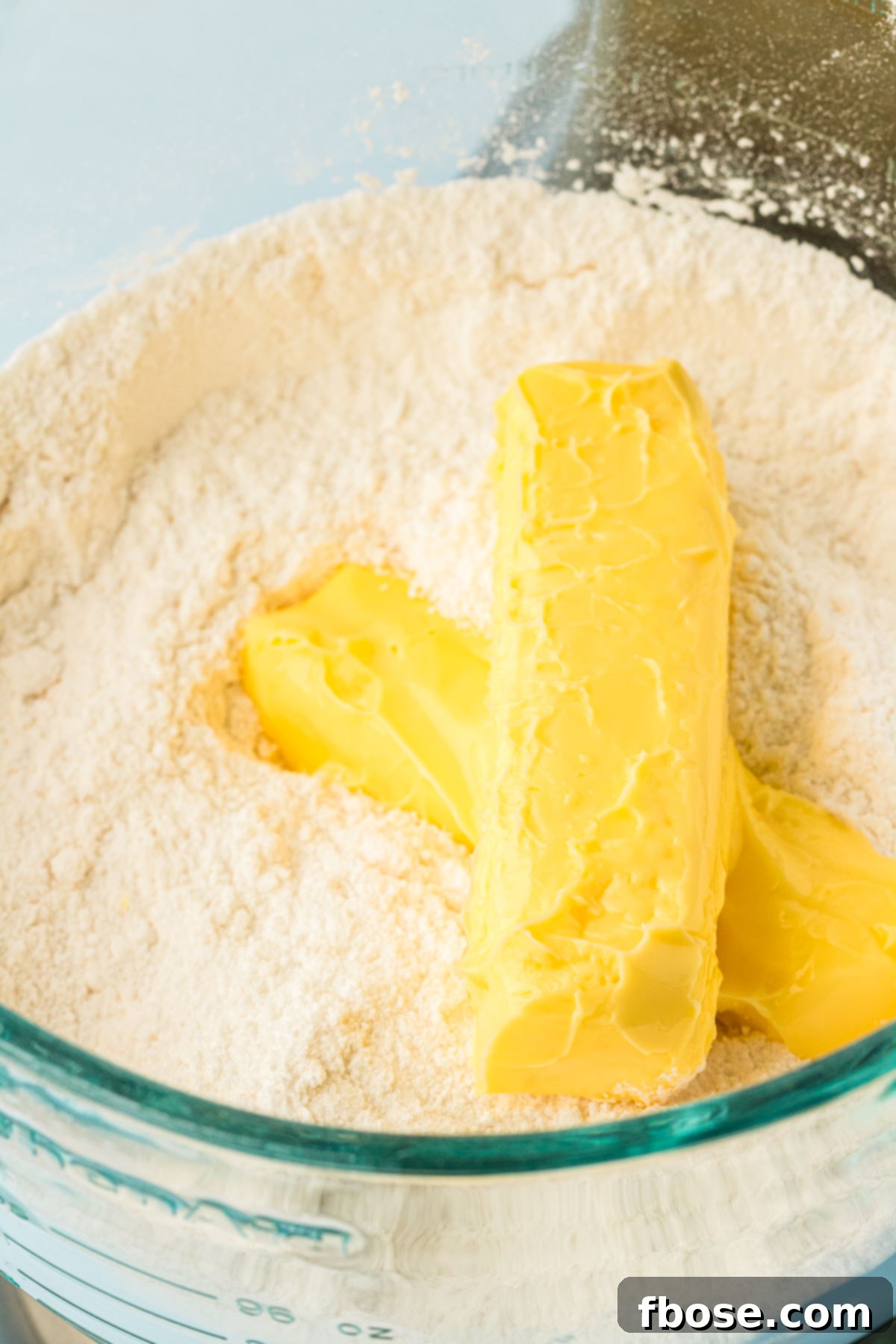 Room temperature butter being carefully added to the mixed dry ingredients in a stand mixer bowl, initiating the reverse creaming process.