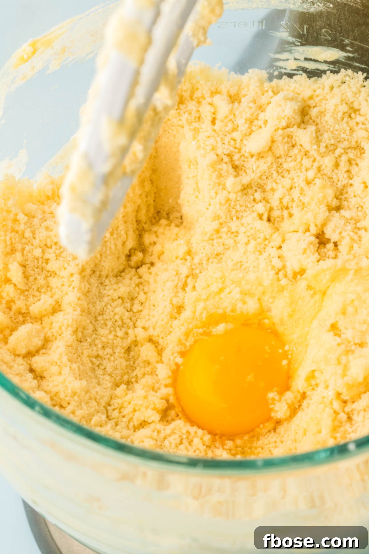 A large egg being cracked and added to the cake mix in the stand mixer, ensuring thorough incorporation for a cohesive batter.