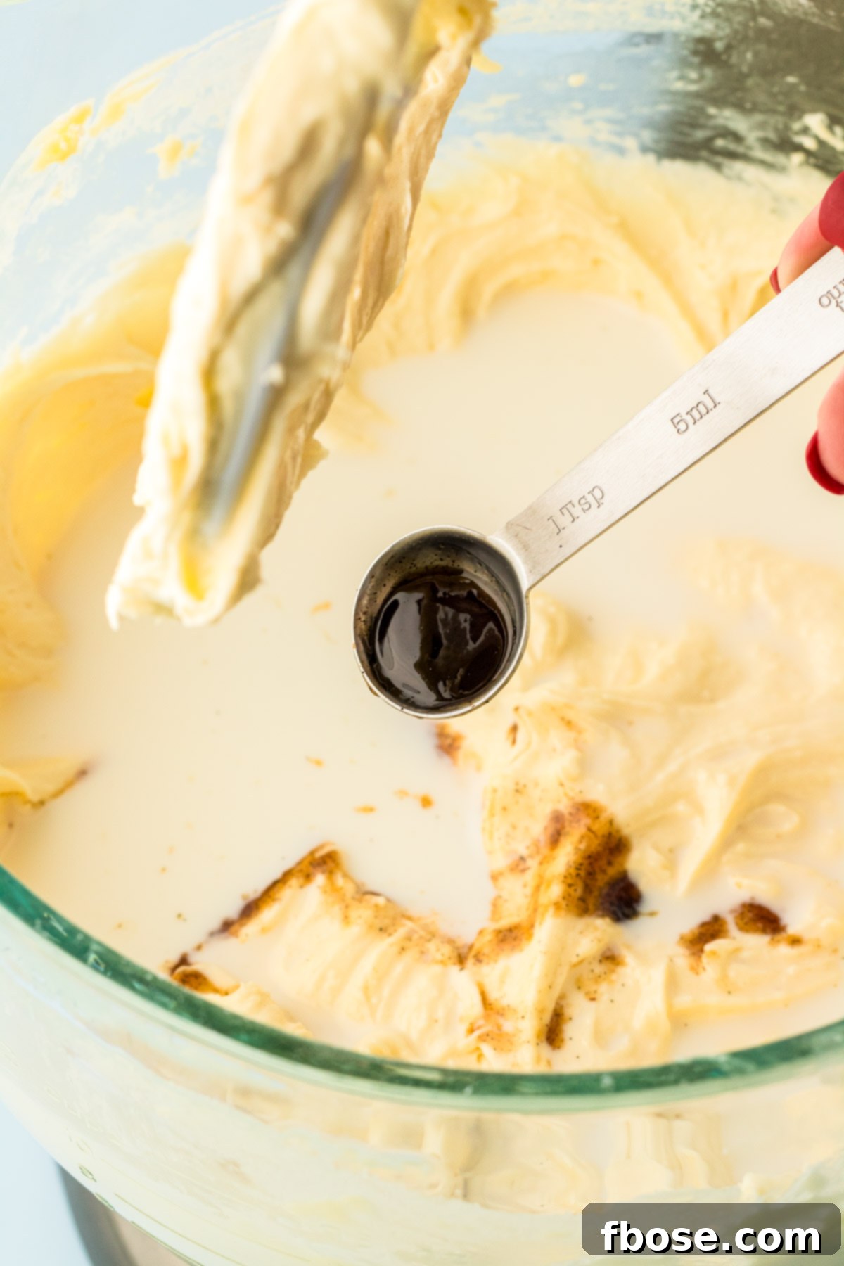 Vanilla bean paste being squeezed into the cake batter, followed by a steady stream of milk, creating a rich and fragrant mixture.