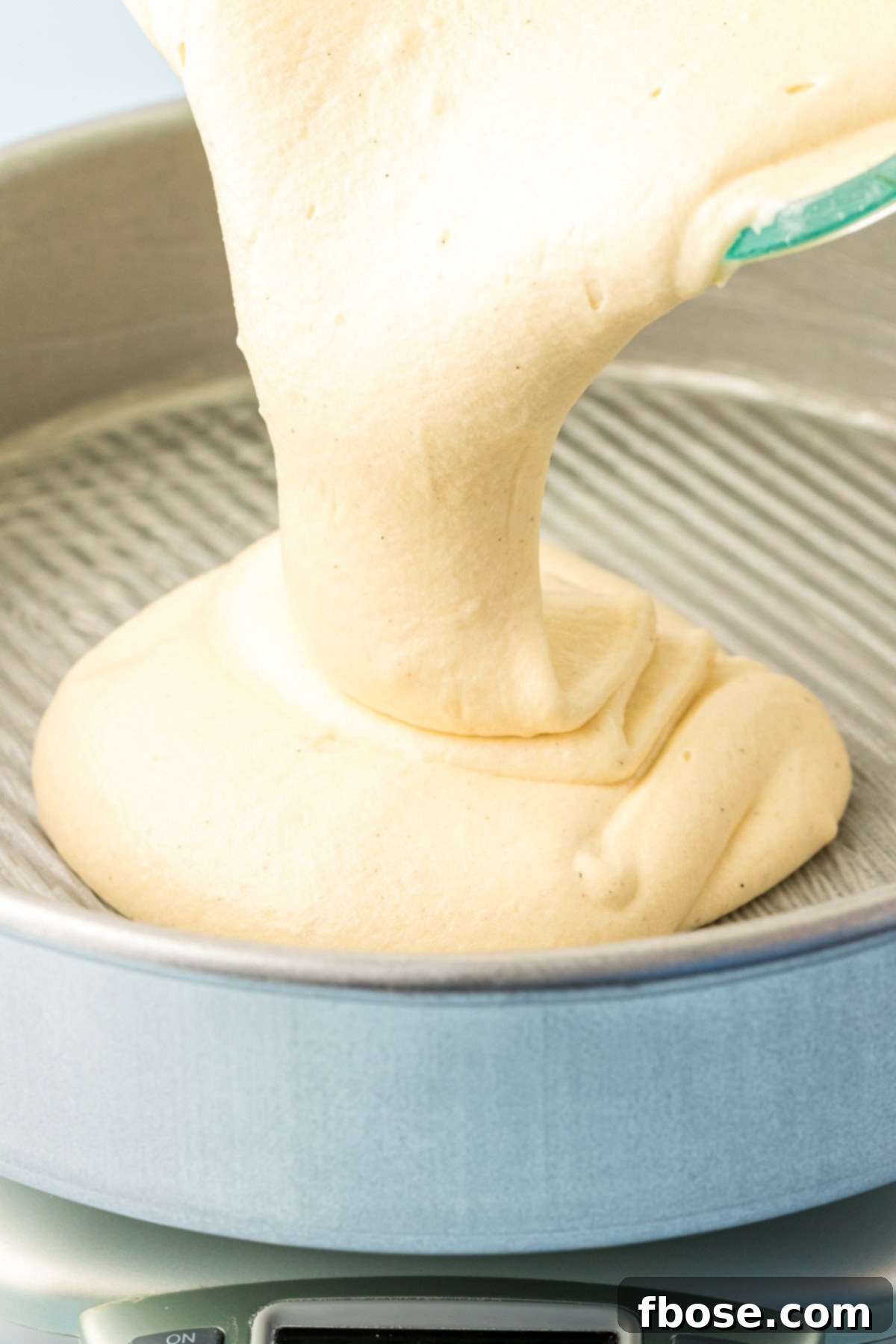 A pristine white cake batter is expertly poured into a round cake pan, ready for baking to achieve light and fluffy layers.