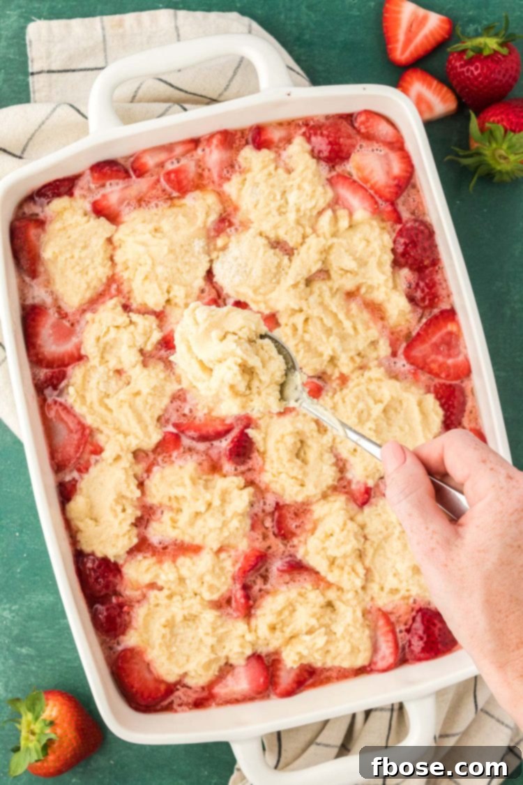 Classic Strawberry Cobbler 15 A woman's hand gracefully dolloping spoonfuls of tender biscuit topping onto a bubbling strawberry cobbler, preparing it for its final bake.