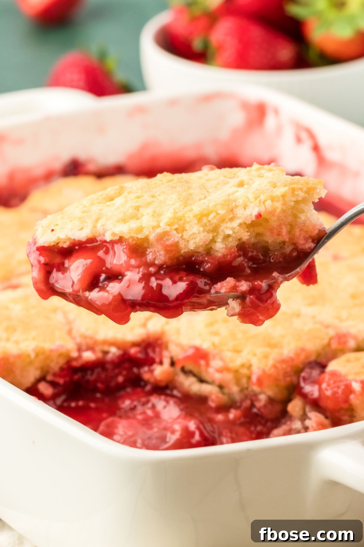 Classic Strawberry Cobbler 16 A serving spoon expertly scooping out a portion of warm, bubbling strawberry cobbler, ready to be enjoyed.