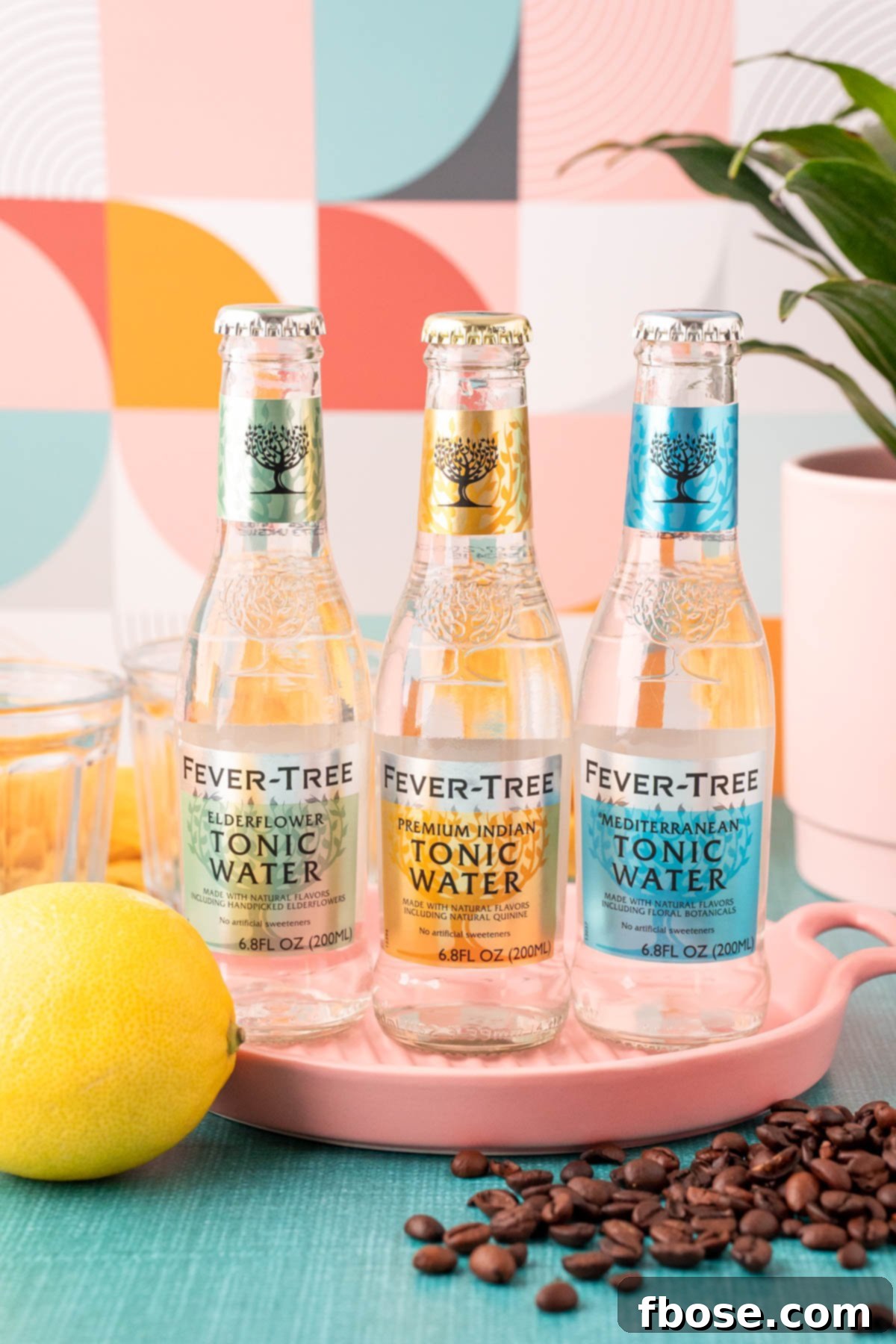 Sparkling Espresso 3 Three bottles of tonic water with a lemon and coffee beans in front of a pink serving tray.