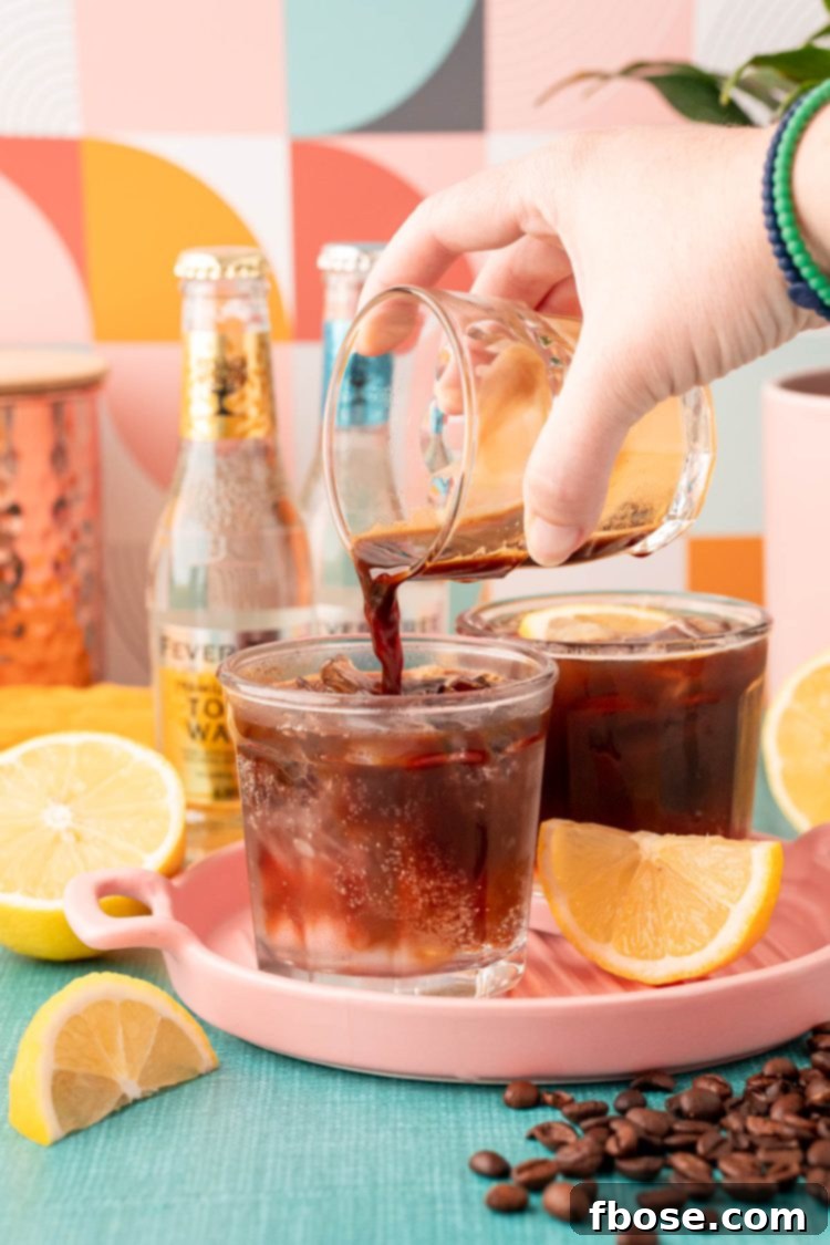A double shot of espresso being poured into a glass with ice and tonic water.