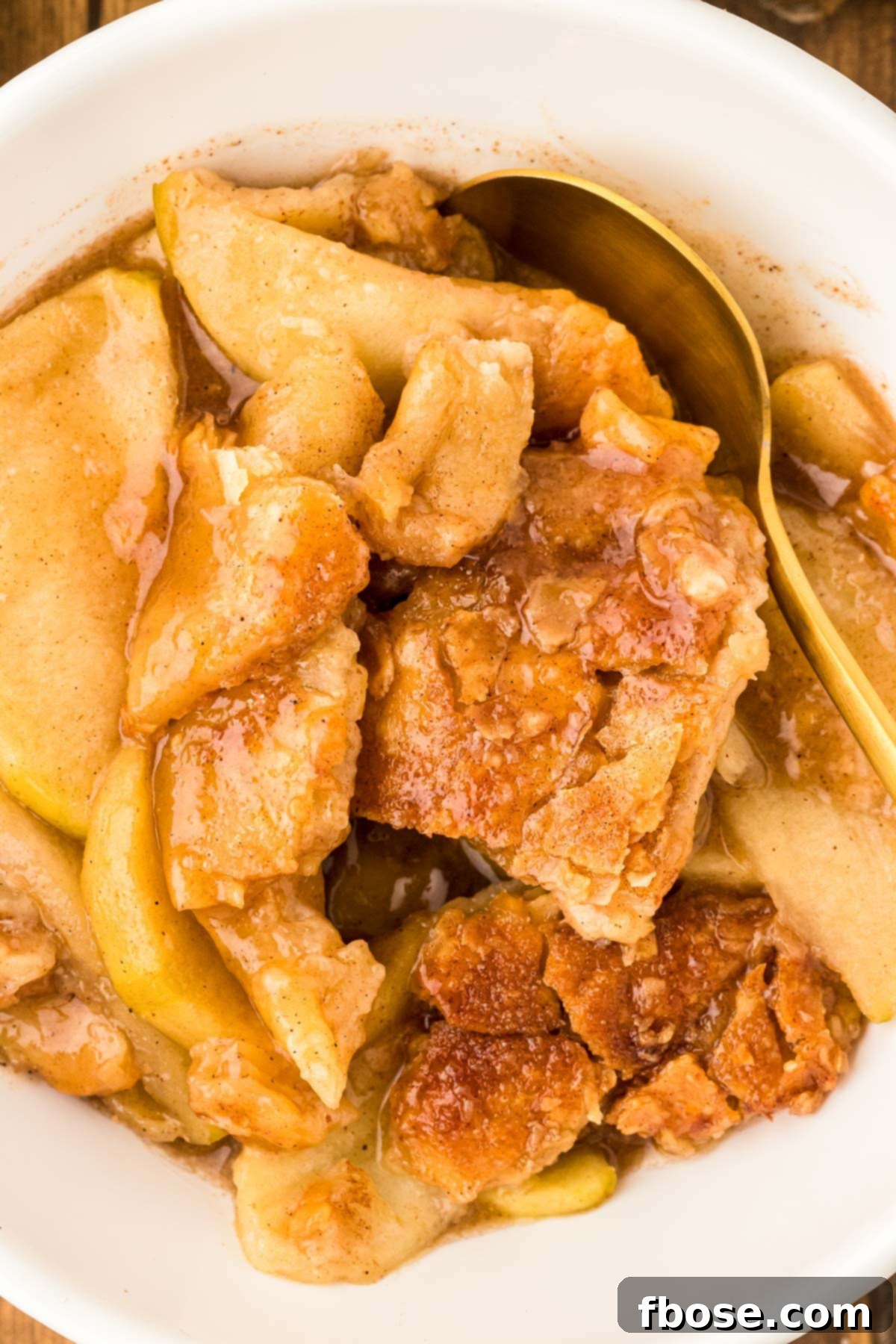 A white bowl filled with apple pan dowdy and a gold spoon.