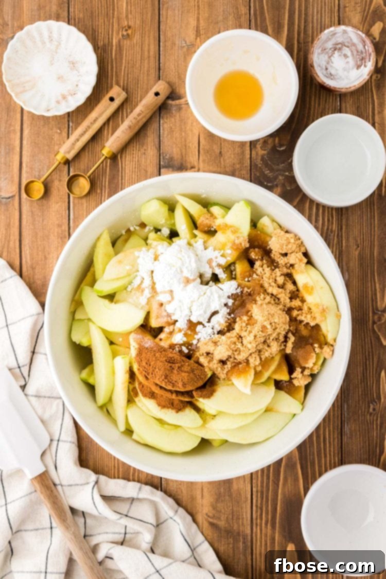 Spices being added to slices apples in a white bowl.