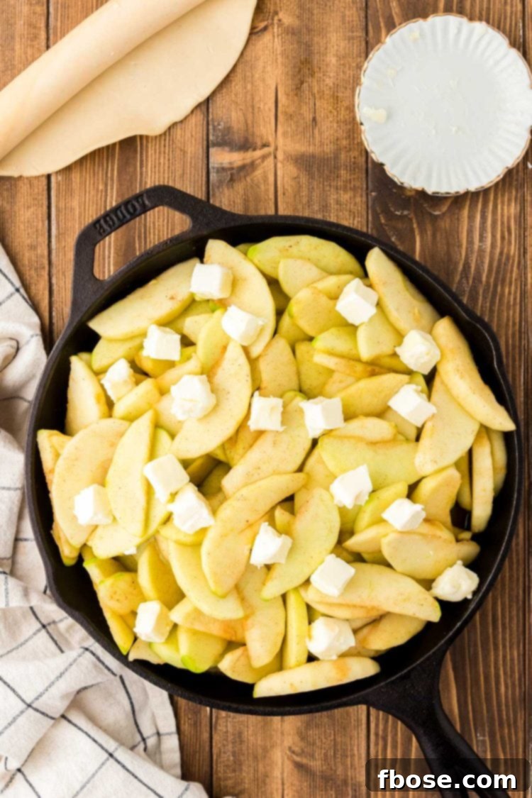Cast iron skillet on a table with sliced apples and butter in it.