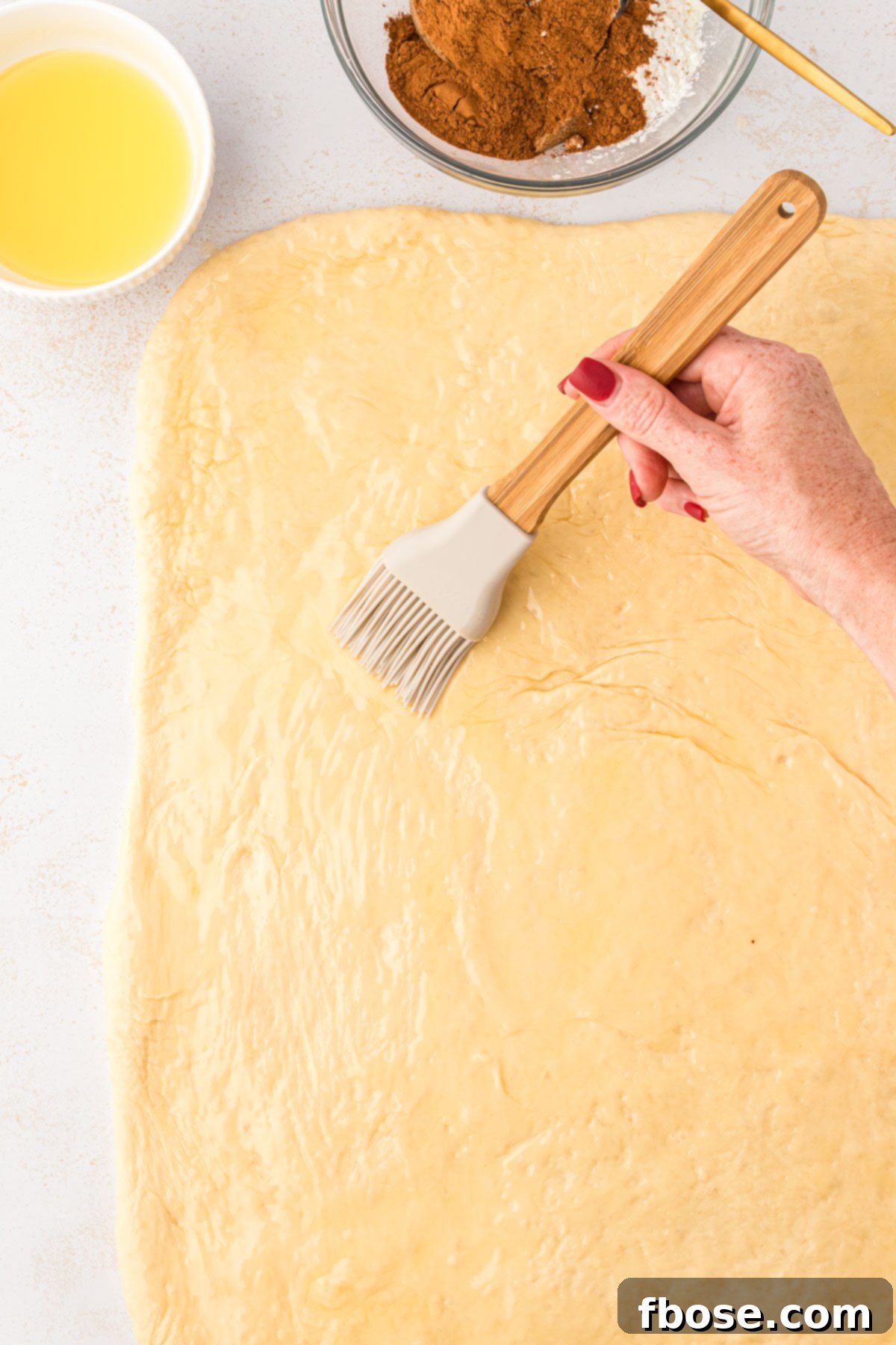 A pastry brush brushing dough with butter to make sweet rolls.