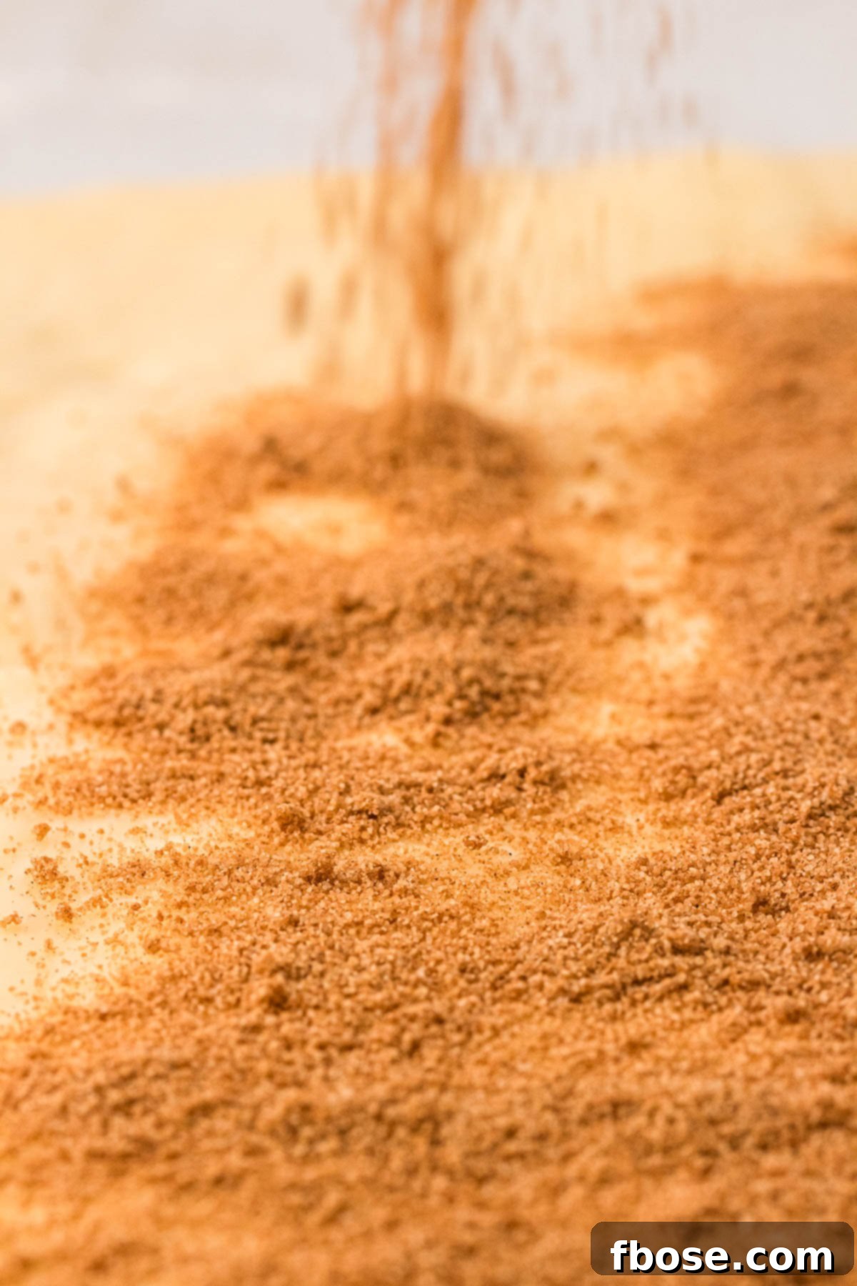 Cinnamon sugar being sprinkled on top of a buttered rectangle of dough.