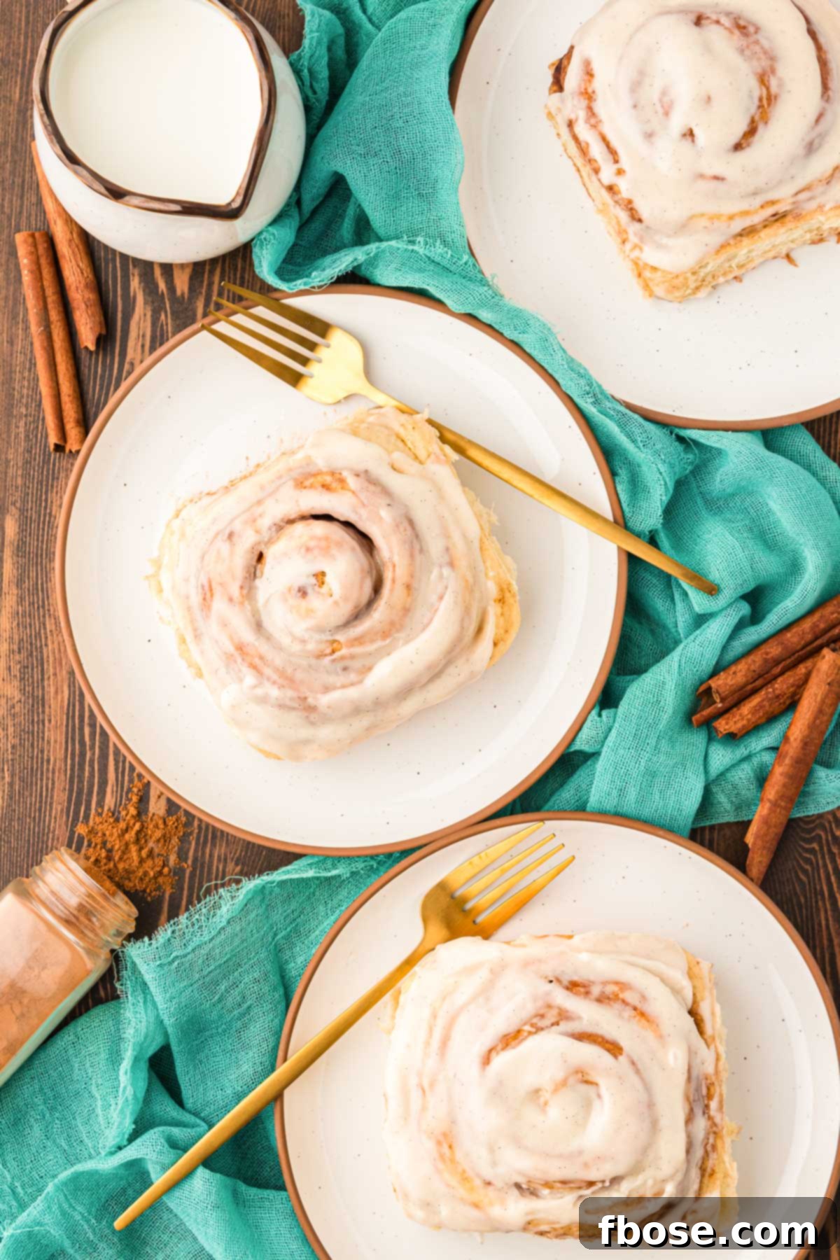 Overhead photo of cinnamon rolls on a plate on a wooden table with a teal napkin.