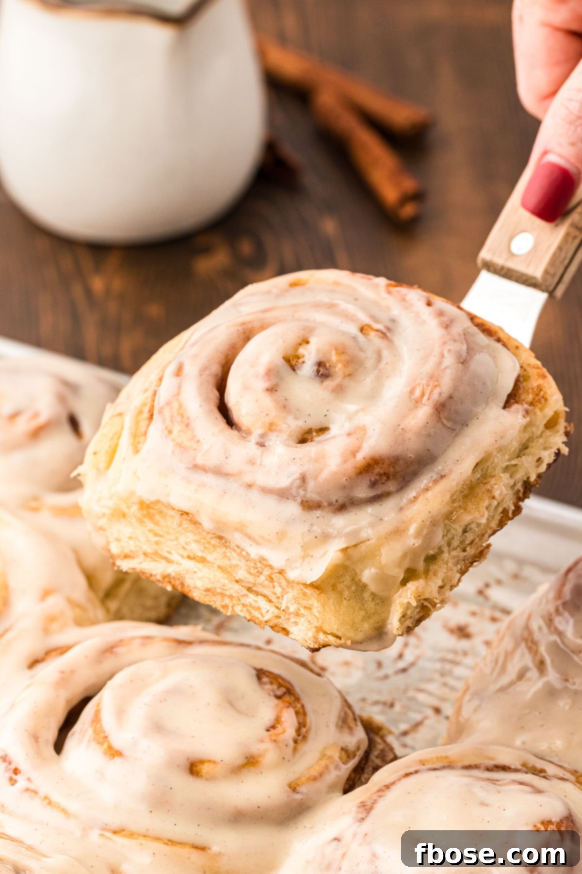 A spatula lifting a cinnamon roll away from the baking pan.