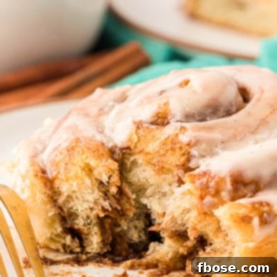A soft cinnamon roll on a white plate with a bite missing out of it.