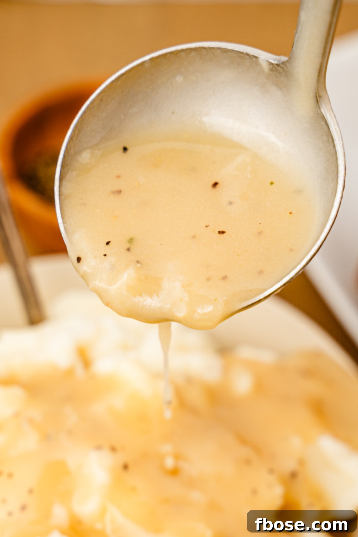 A ladle with turkey gravy pouring on mashed potatoes.