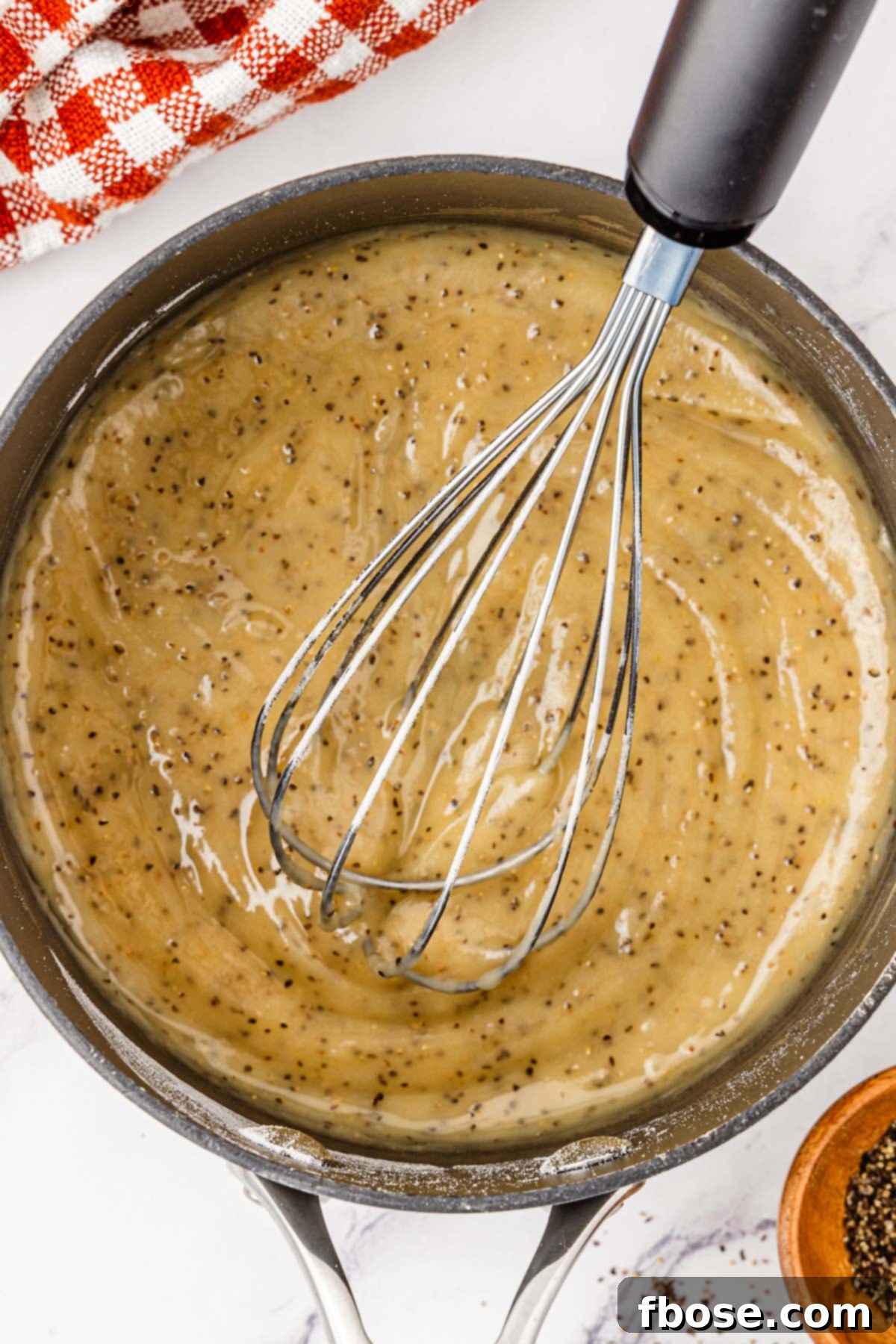 Flour, butter, and black pepper being whisked in a saucepan.