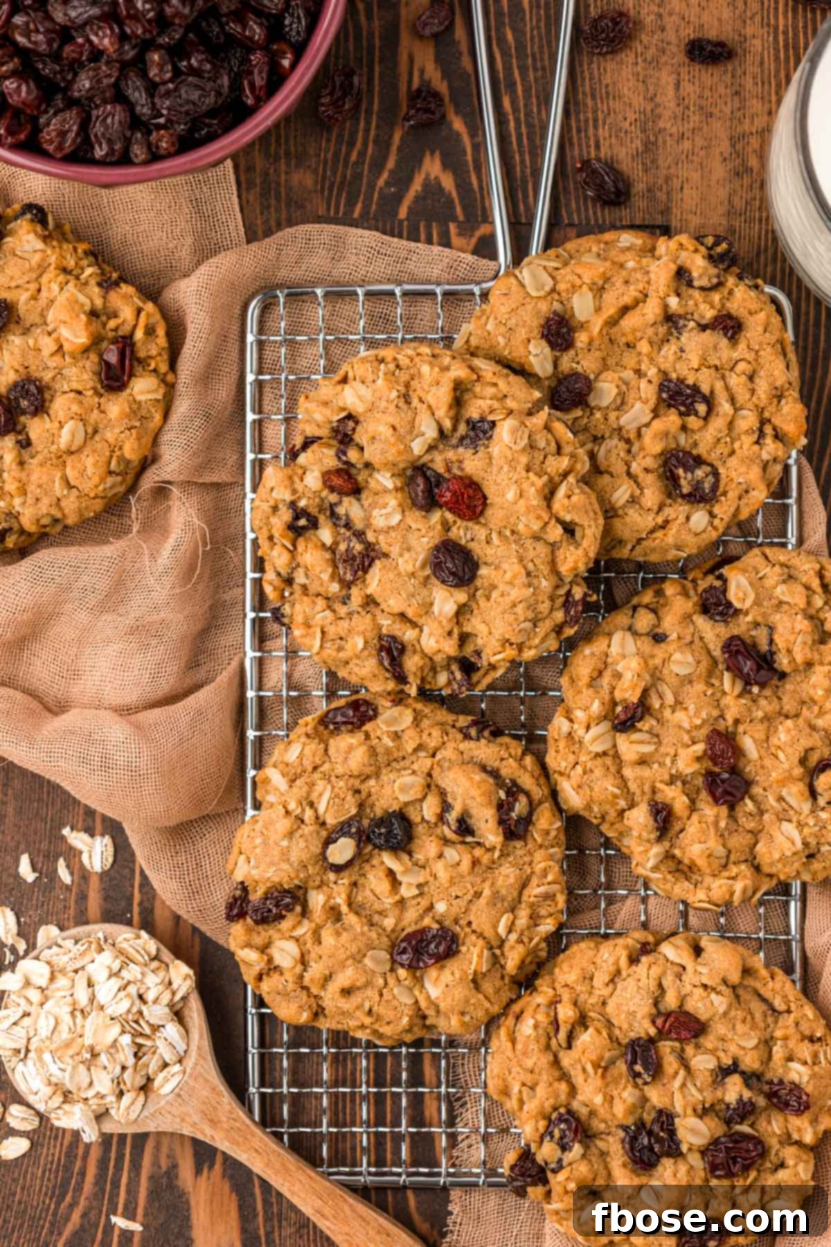 Overhead photo of golden-brown oatmeal raisin cookies cooling on a wire rack against a rustic wooden backdrop.