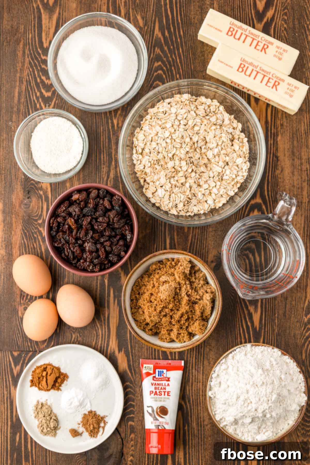 A rustic wooden table displaying all the fresh ingredients needed to bake a batch of homemade oatmeal raisin cookies.