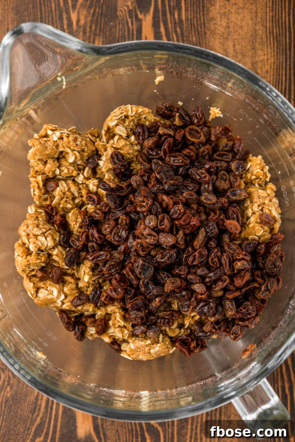 Juicy, rehydrated raisins being gently folded into a bowl of rich, golden-brown oatmeal cookie dough.