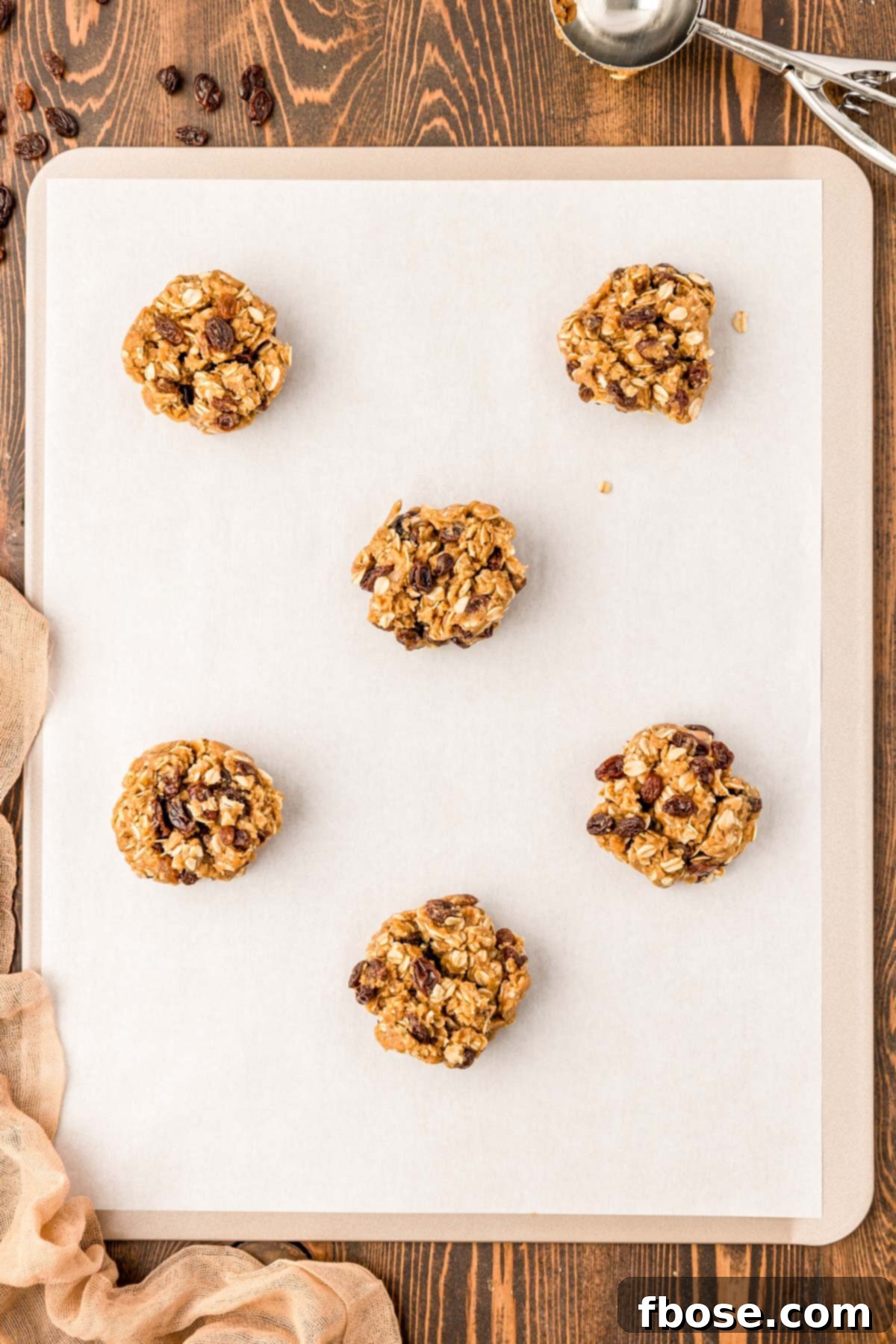 Perfectly portioned oatmeal raisin cookie dough balls on a parchment-lined baking sheet, ready for the oven.