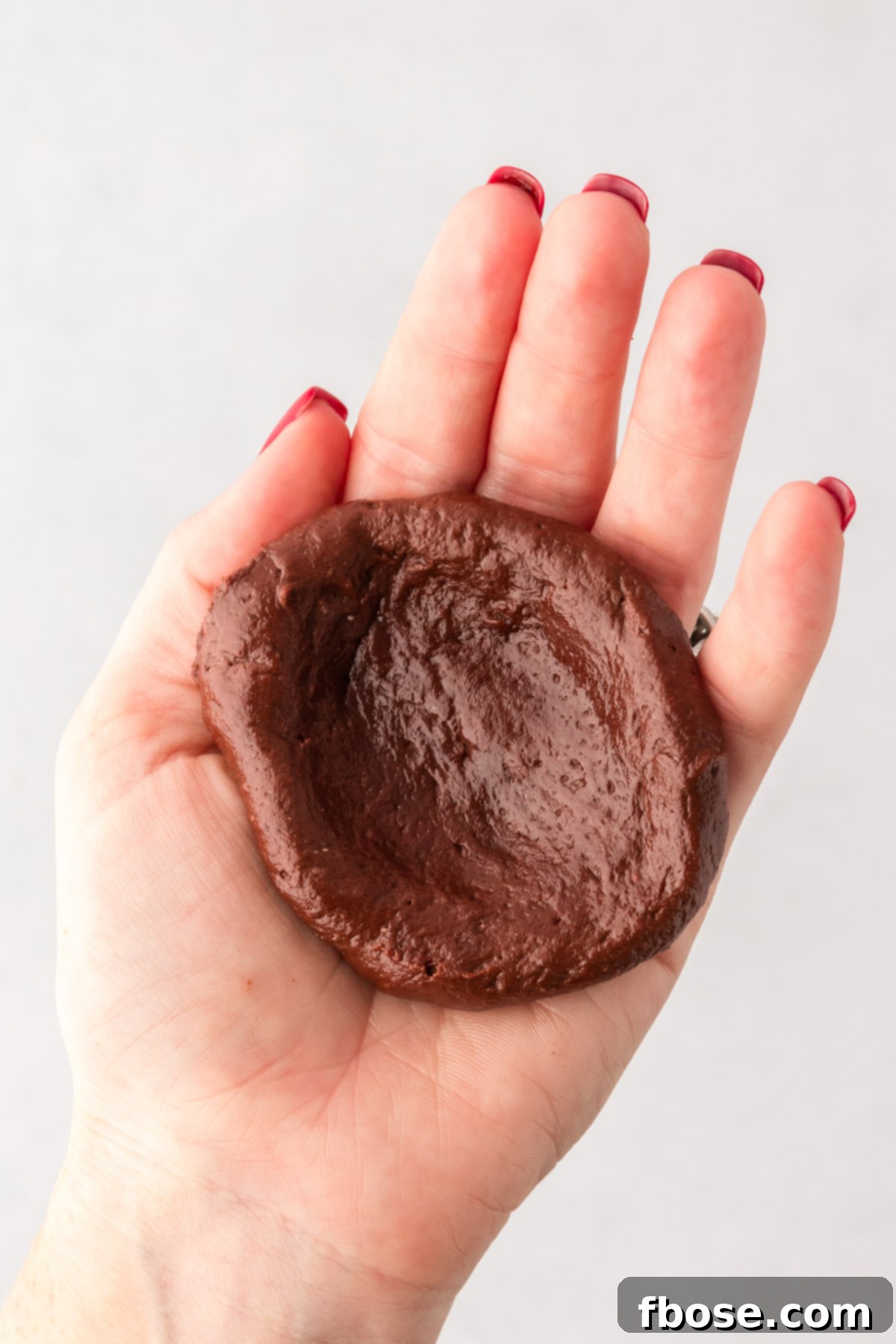 Chocolate cookie dough in a woman's hand in a bowl shape.