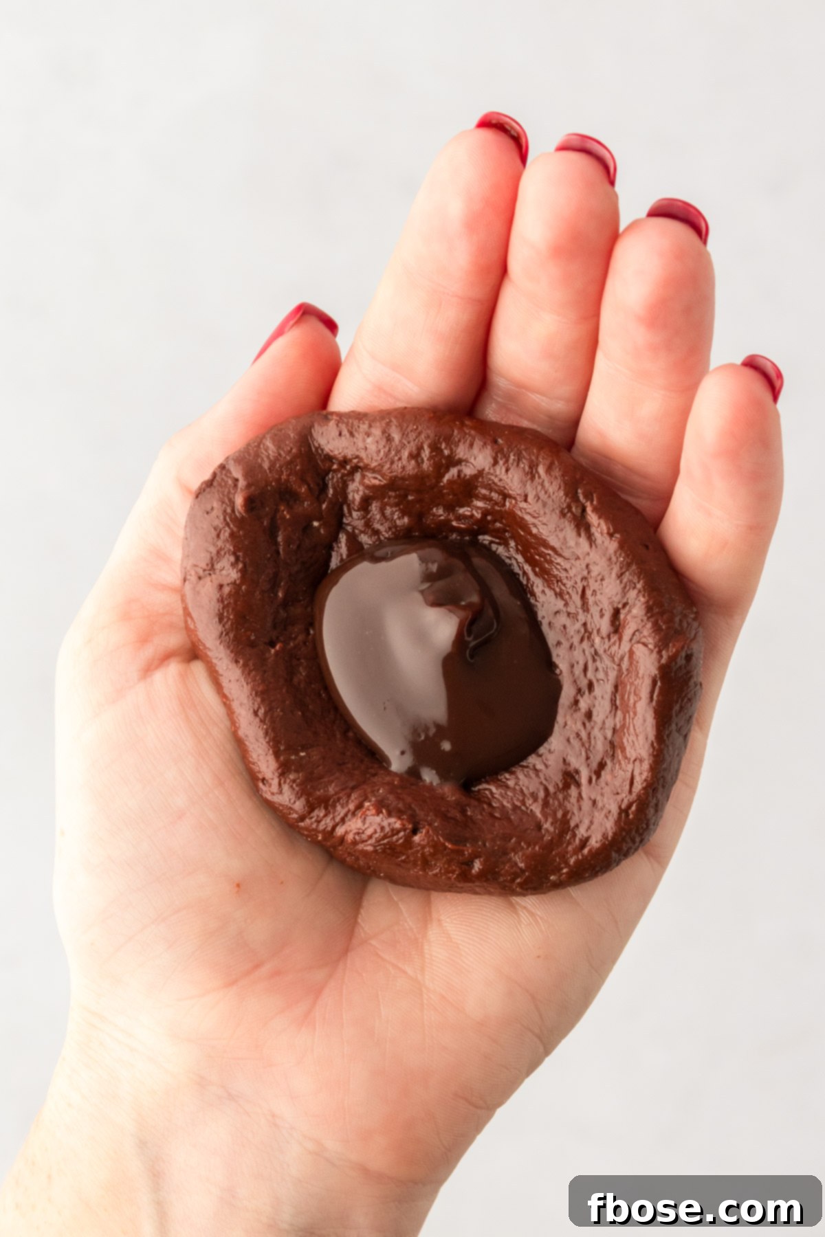 A scoop of hot fudge in the center of chocolate cookie dough in a woman's hand.