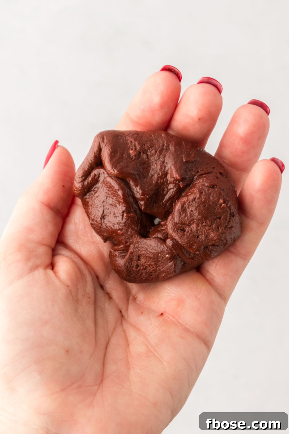 A ball of chocolate cookie dough being wrapped around hot fudge.