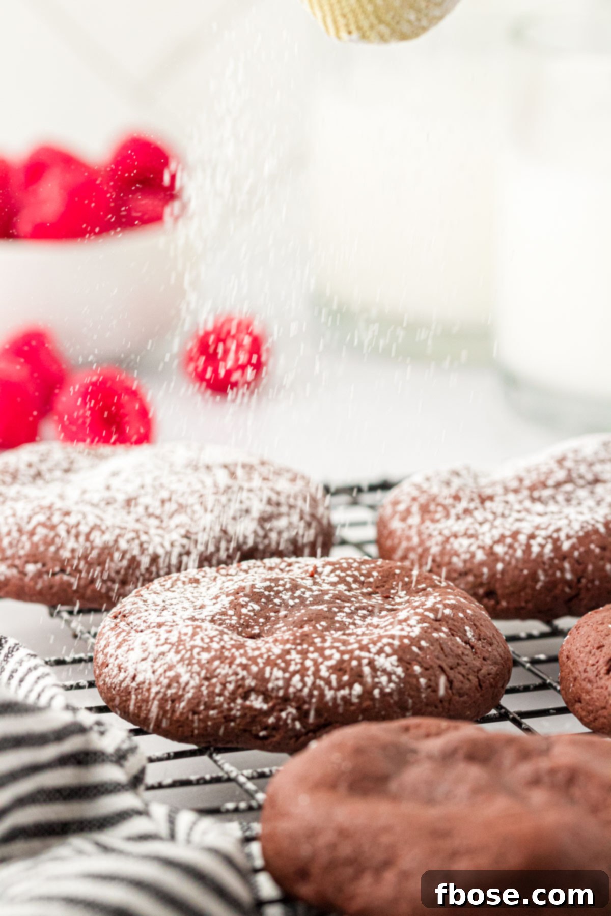 Chocolate cookies on a wire rack being dusted with powdered sugar.