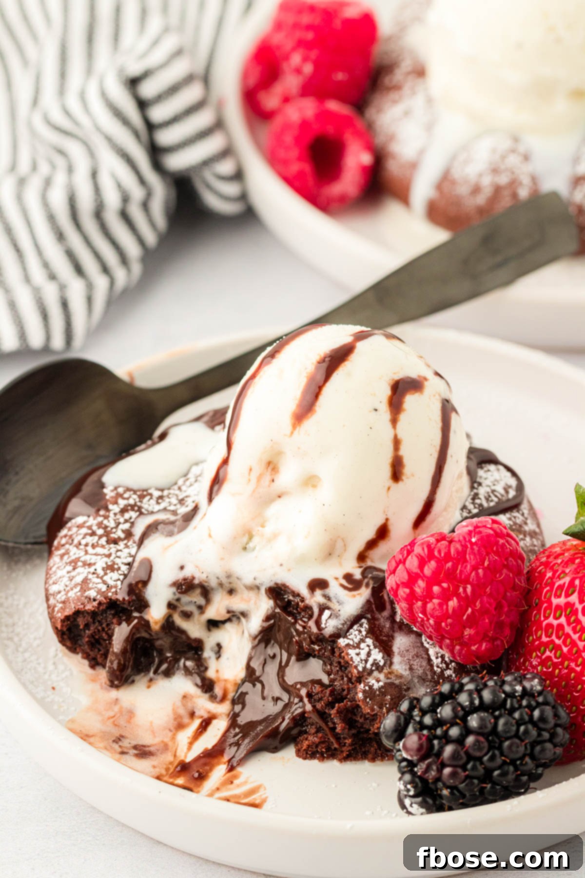 A large lava cake cookie on a white plate with berries around it and a scoop of vanilla ice cream on top.