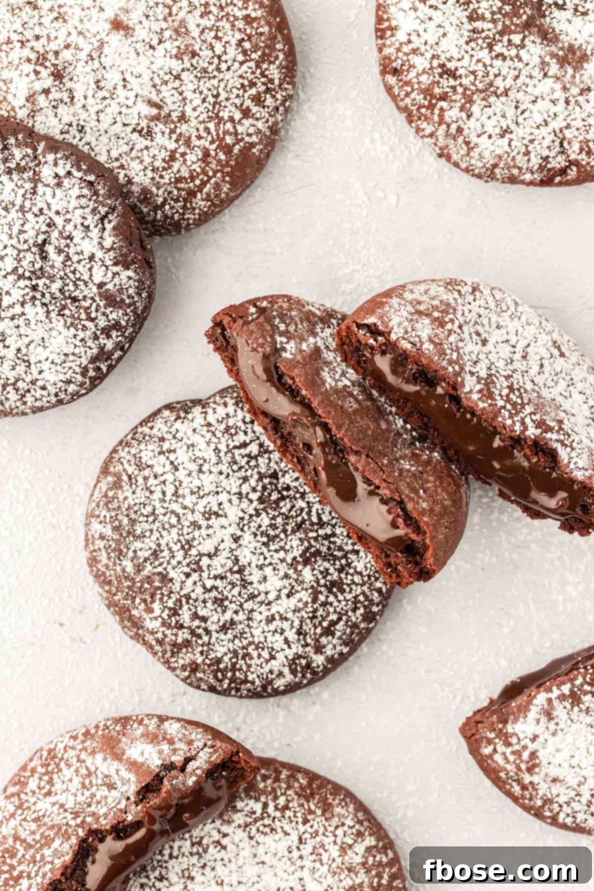 Overhead photo of molten lava cake cookies on a white table, some broken in half to reveal the gooey center.
