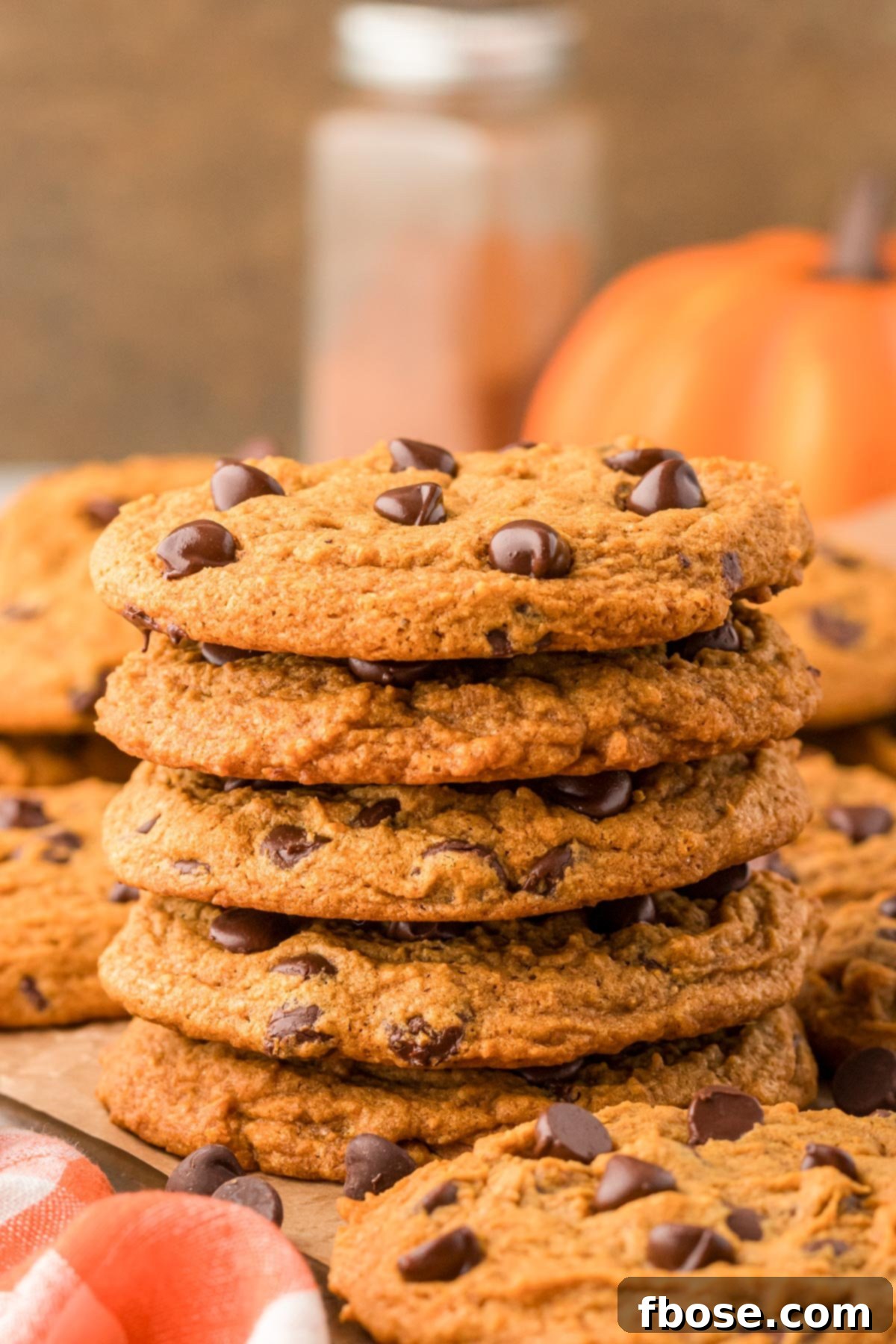 Velvety Pumpkin Chocolate Chip Delights 9 A tall stack of chewy pumpkin chocolate chip cookies, garnished with chocolate chips, on a wooden table.