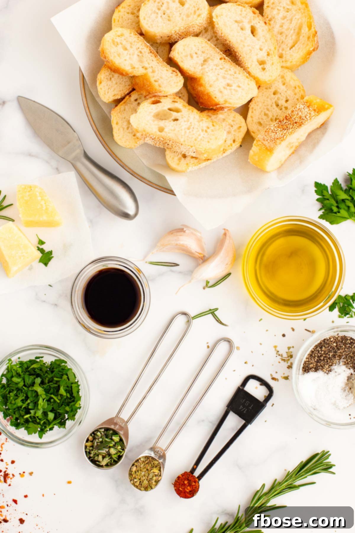 Overhead photo of ingredients to make olive oil bread dip on a white table.