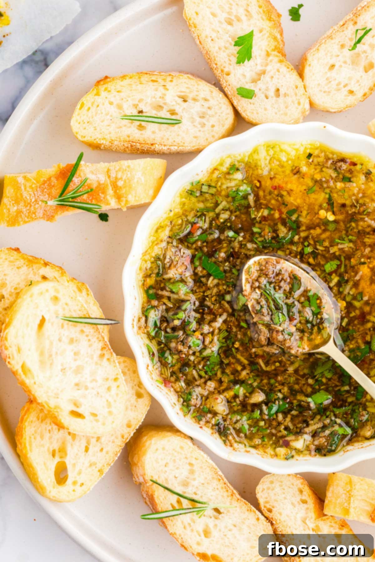 Overhead photo of slices baguette on a white plate with a dish of dipping oil and herbs.