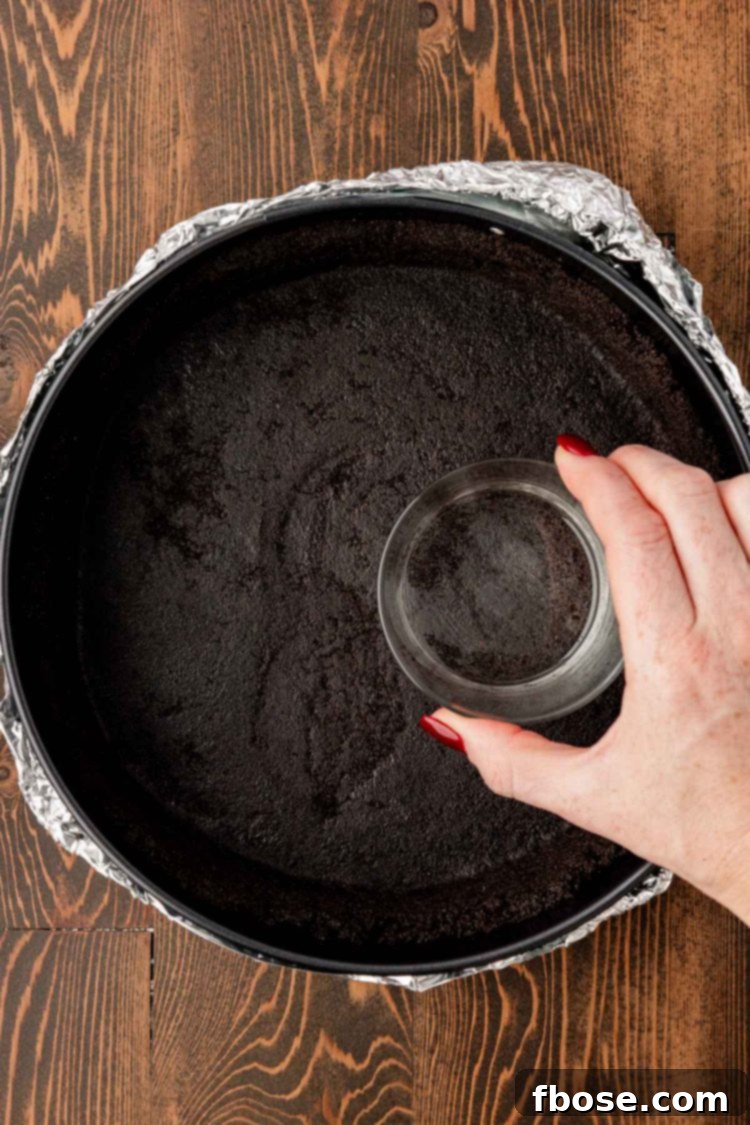 Gourmet Coffee Cheesecake 6 A woman's hand pressing a glass into the bottom of a springform pan filled with oreo crust.
