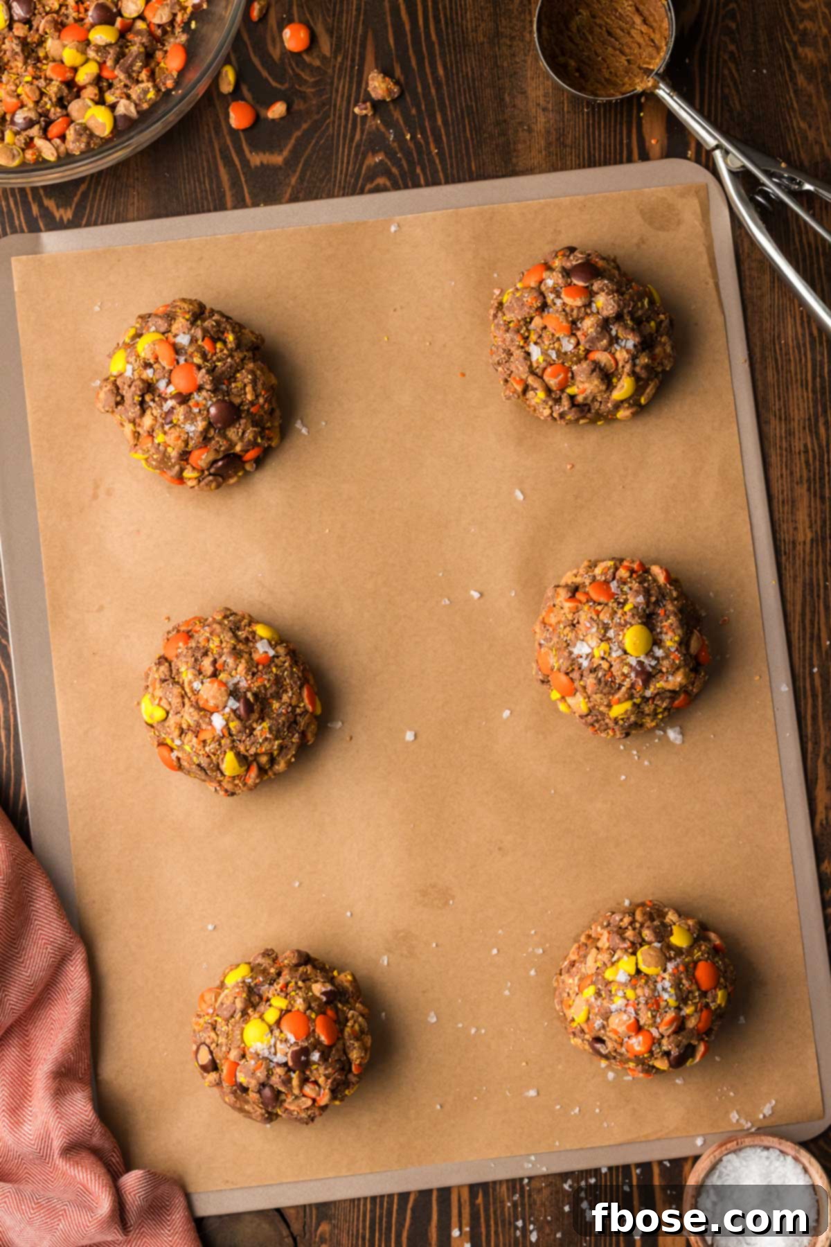 Large, unbaked Gideon's Bakehouse Peanut Butter Cold Brew cookies on a parchment-lined baking sheet, covered in candy.