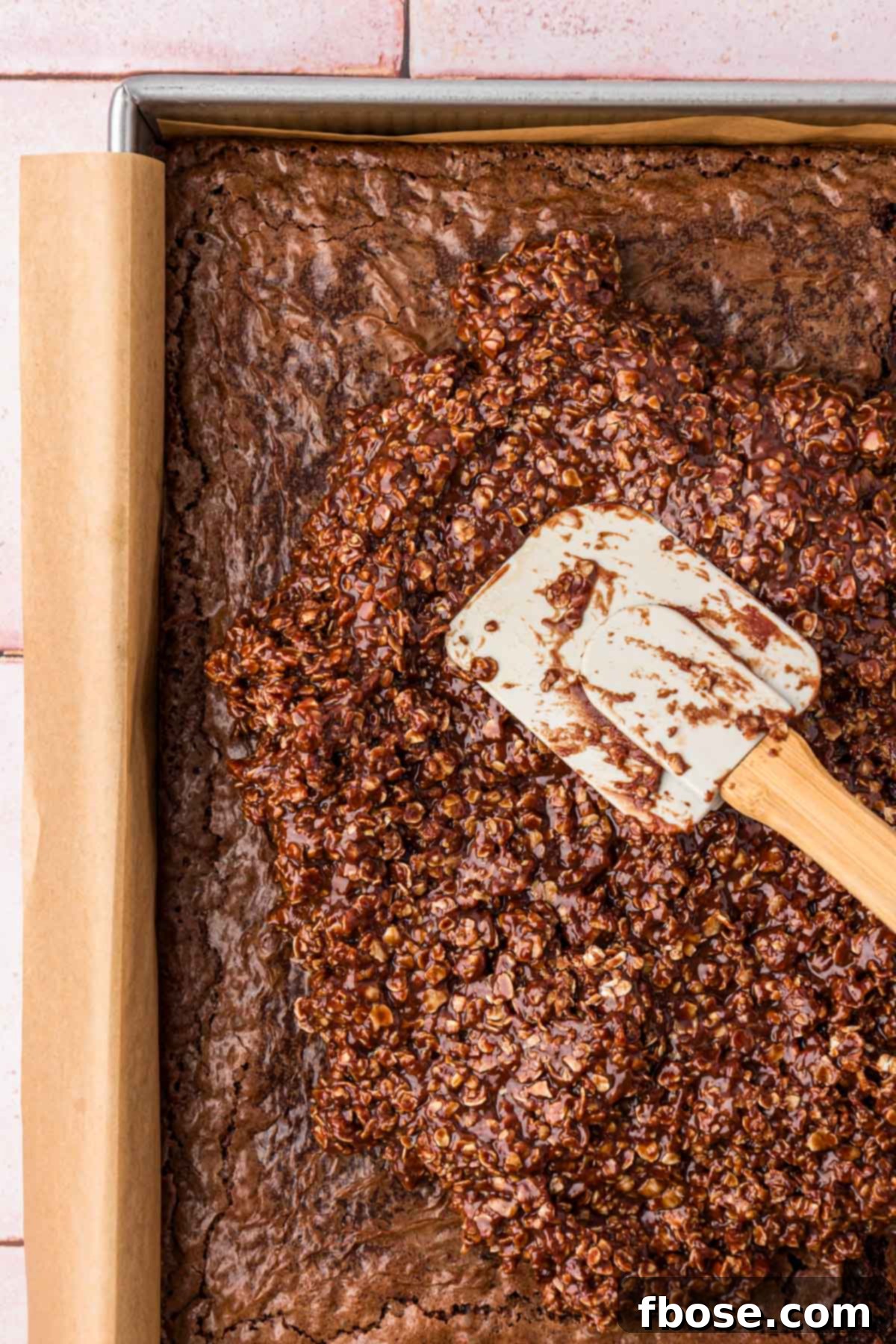 Effortless Fudgy Cookie Brownie Bars 6 No bake cookie mixture being spread over the top of cooled brownies in a pan.