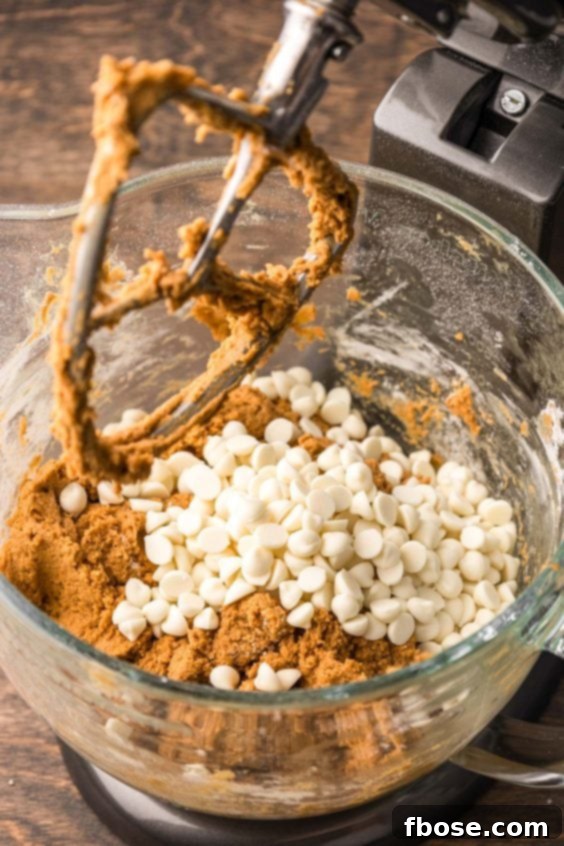 White chocolate chips being added to pumpkin cookie dough.