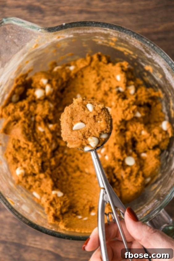 A cookie scoop scooping dough out of a glass bowl.