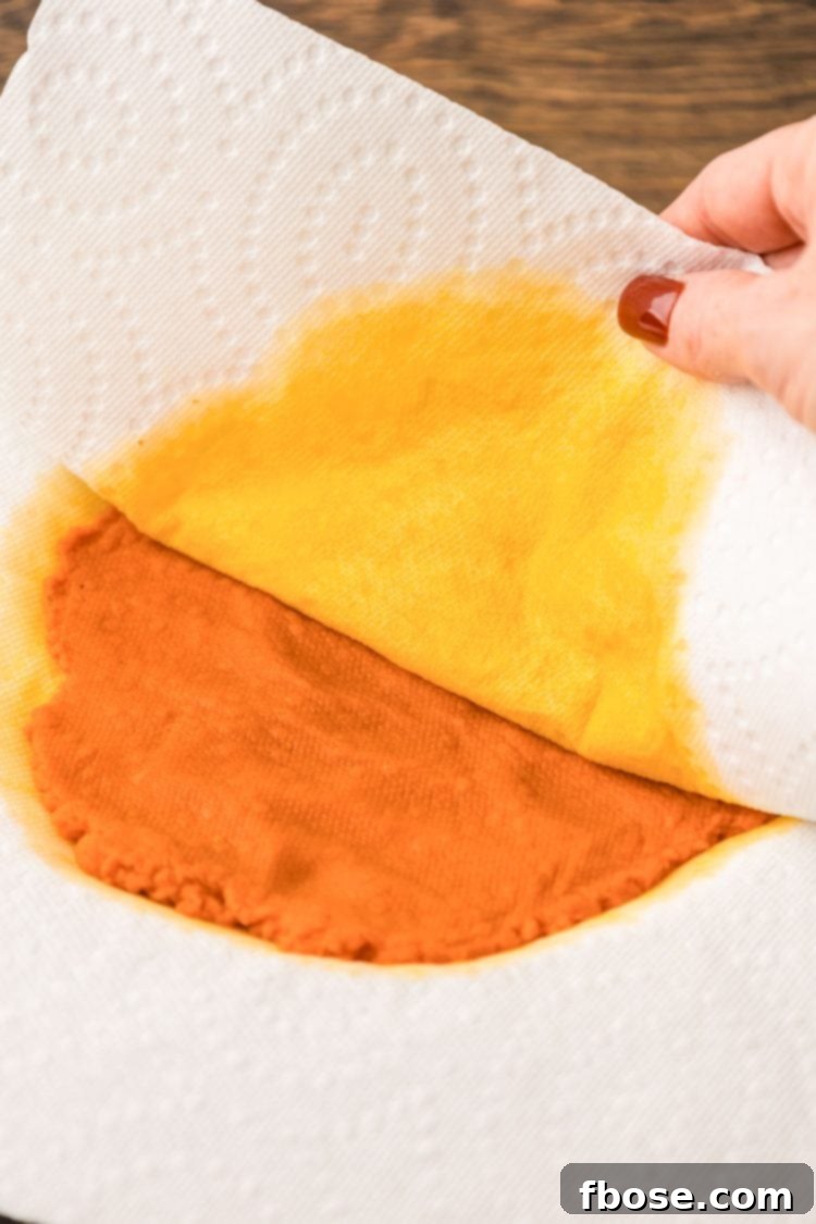 Paper towel pulling away from pumpkin puree after soaking up moisture, revealing a drier pumpkin.