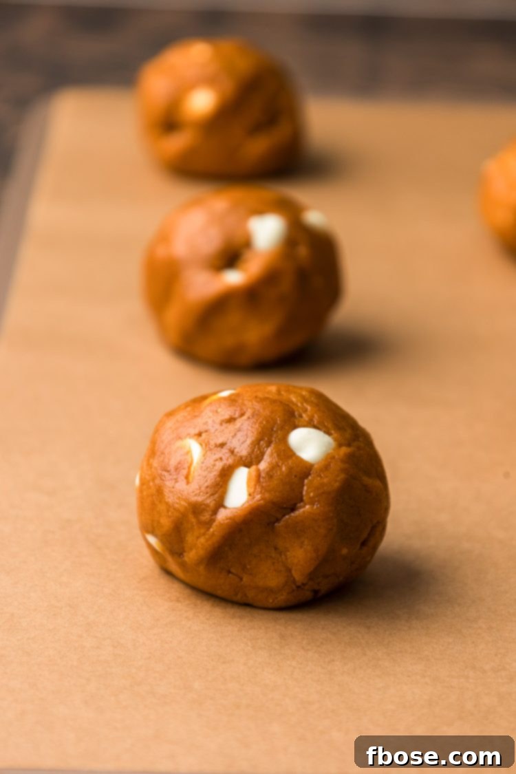 Pumpkin white chocolate chip cookies baking on a parchment-lined cookie sheet.