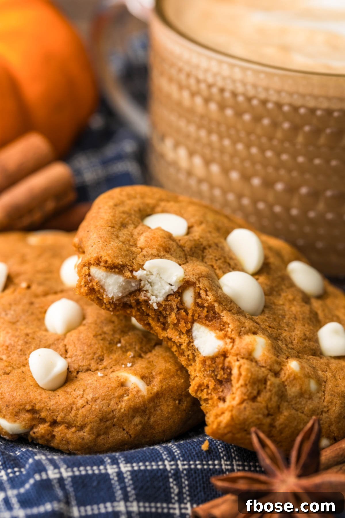 Pumpkin White Chocolate Chip cookies on a blue napkin, with one cookie missing a bite, showing its soft interior.
