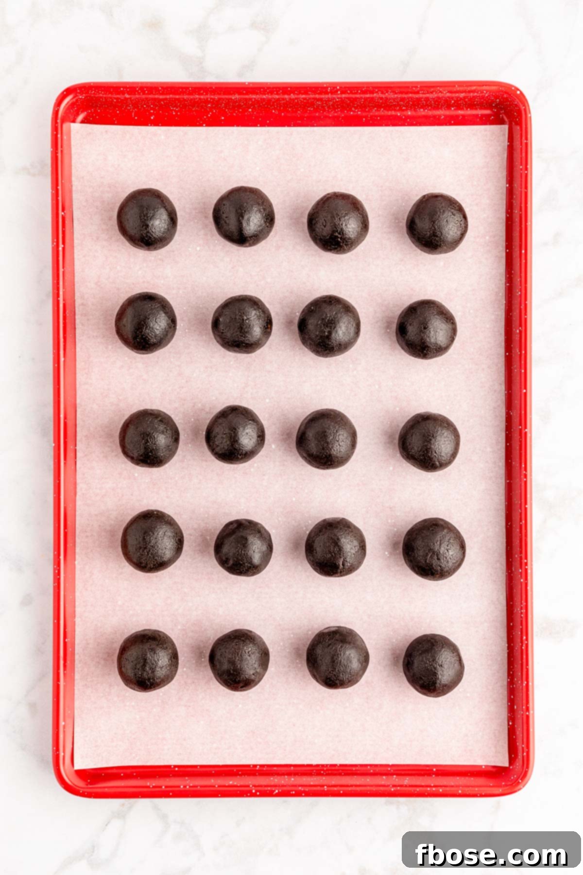 Oreo balls neatly rolled and arranged on a parchment-lined baking sheet, chilling before dipping.